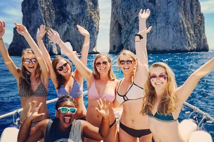 Smiling group of friends on a Capri boat tour near Faraglioni rocks, enjoying the sun and sea adventure from Sorrento.