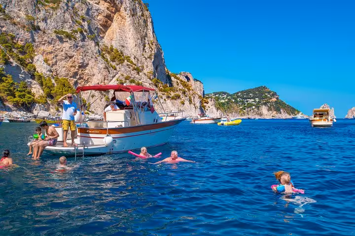 Tourists swimming near a boat in the clear blue waters of Capri on a small group excursion from Sorrento.