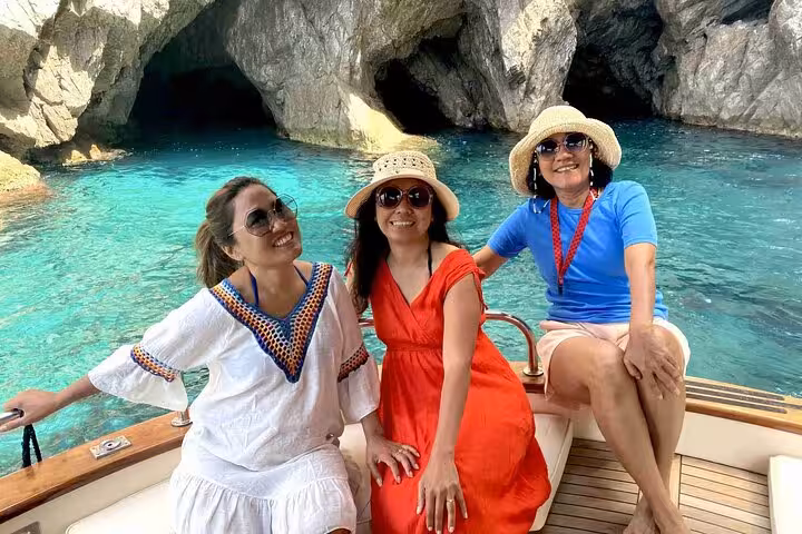 Three women relaxing on a boat near the vibrant blue waters of Capri's famous grotto.
