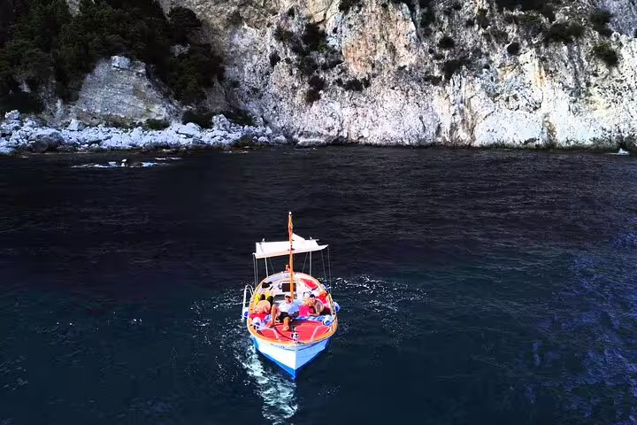 Private full-day Capri boat tour cruising crystal-clear sea near limestone cliffs, relaxing on board