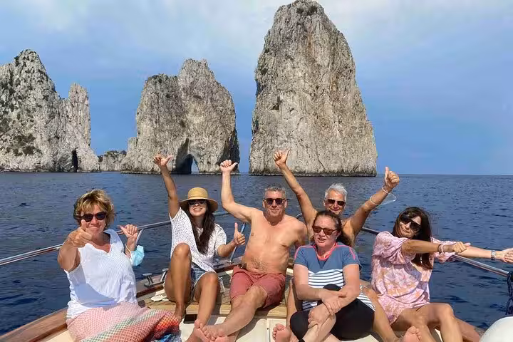 Group enjoying a Capri boat tour with iconic Faraglioni rocks in the background on a sunny day.