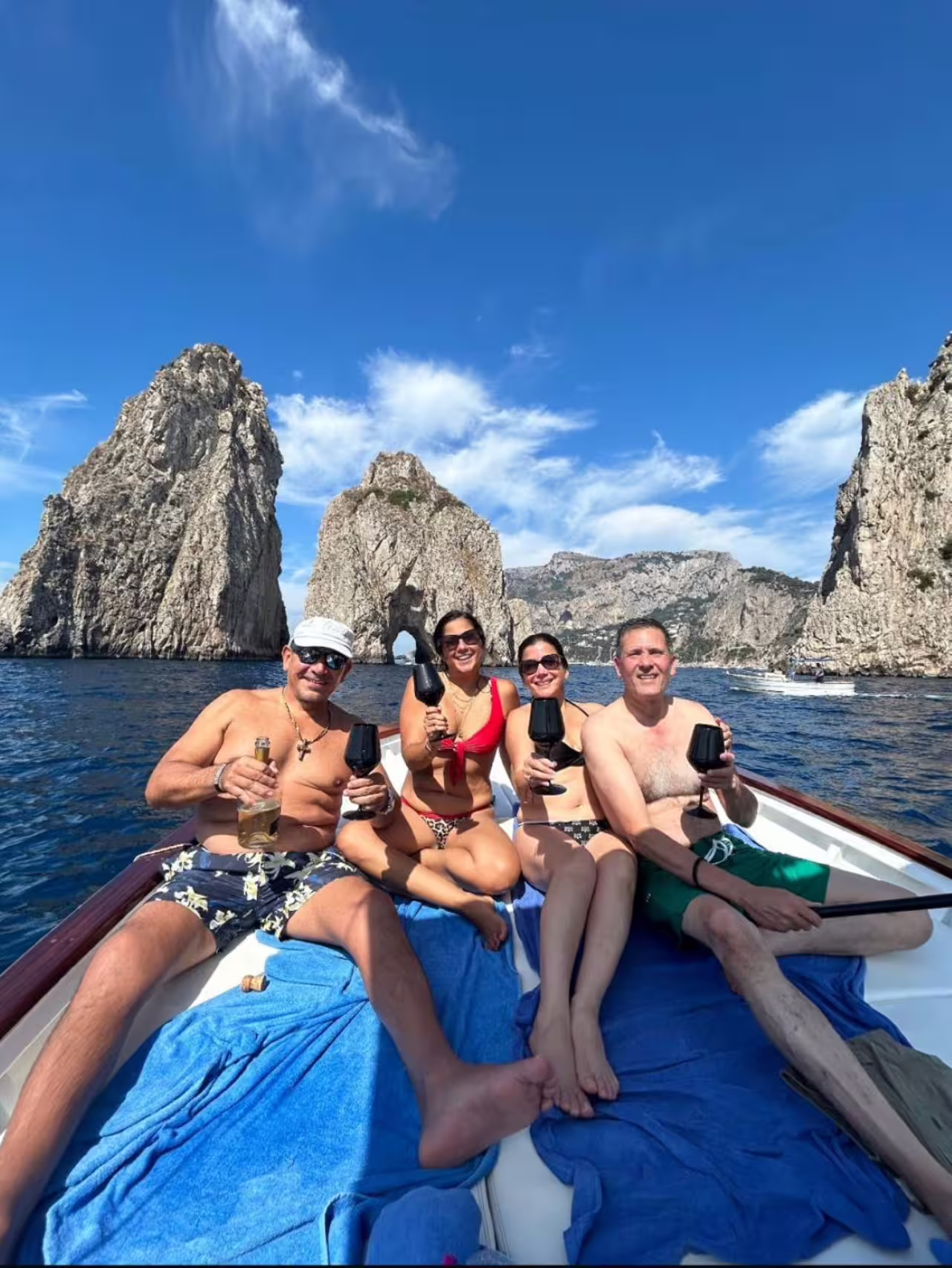 Friends toasting with drinks on a private boat tour near Capri's scenic Faraglioni rocks, enjoying serene ocean views.