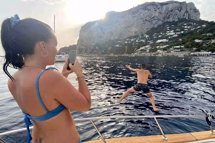 Woman photographs as a man jumps into the clear waters near Capri's stunning coastline.