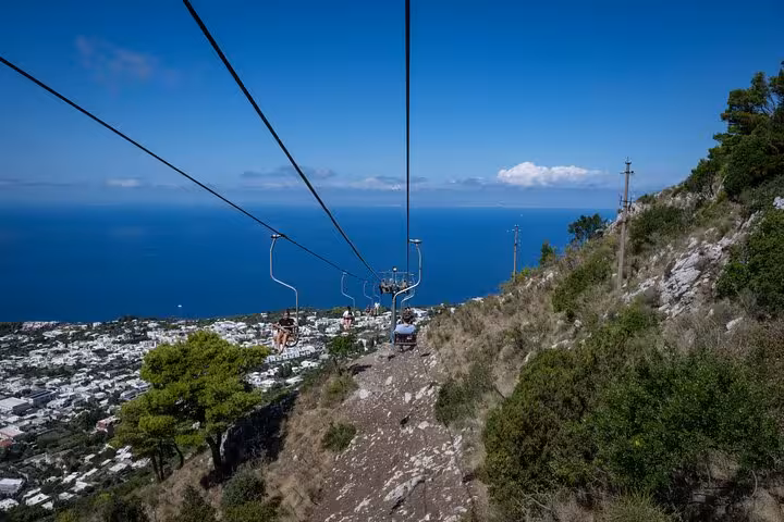 Scenic chairlift offering panoramic views of Capri's coastline and azure sea on a guided tour from Naples.