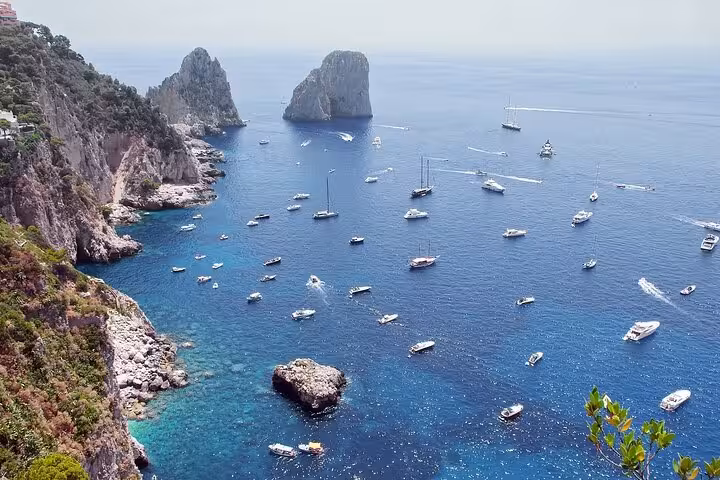 Scenic view of Capri's coastline with boats and the iconic Faraglioni rock formations in the azure sea.