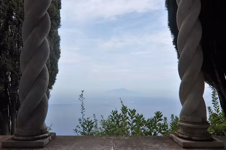 Breathtaking view of the sea and distant mountains framed by twisted columns and lush greenery on Capri.