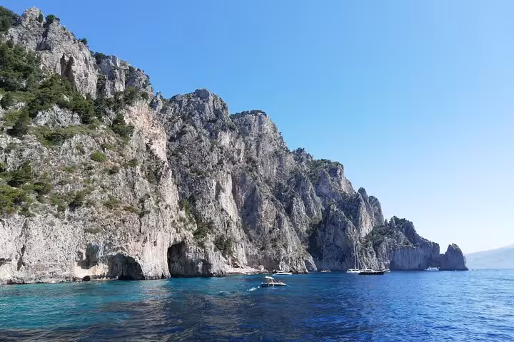 Picturesque view of Capri's rugged coastline with boats near the iconic Faraglioni rocks.