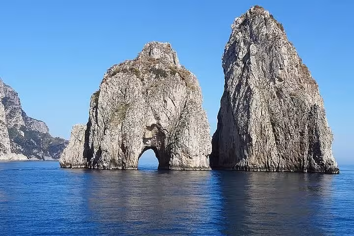 Iconic Faraglioni rocks rising from the sea under a clear blue sky on a Capri island tour.
