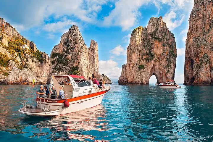 Tourists enjoy a scenic boat tour near the iconic Faraglioni rocks in Capri, offering stunning views from Amalfi waters.