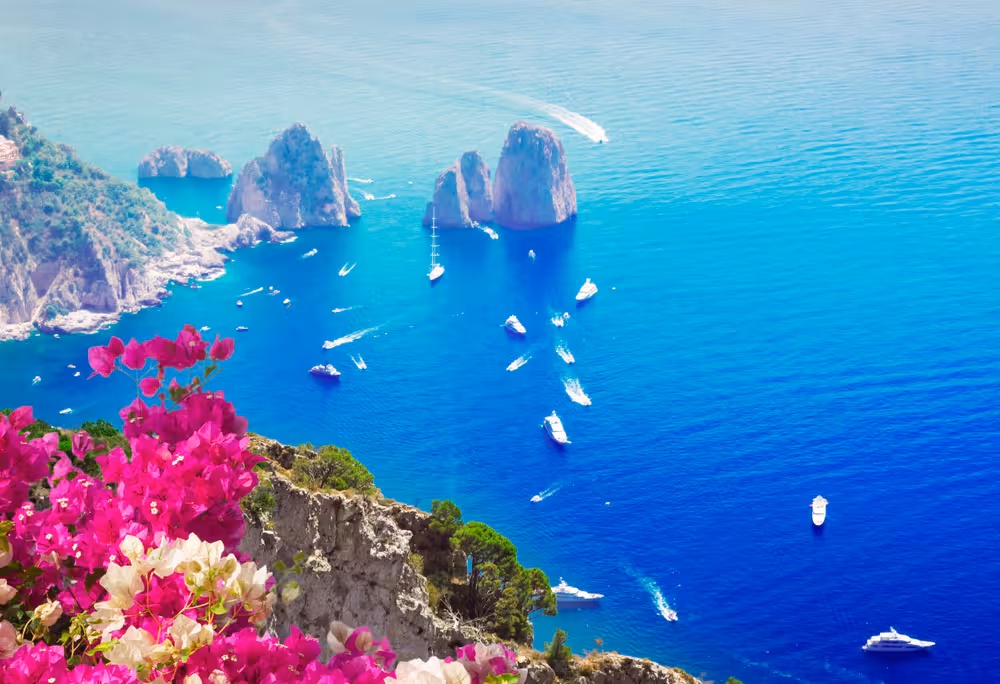 Breathtaking view of Capri's Faraglioni rocks with vibrant bougainvillea, ideal for a scenic boat tour from Rome.