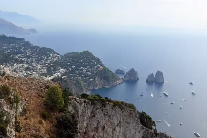 Breathtaking panorama of Capri's rugged cliffs and Faraglioni rocks surrounded by sailboats on the Mediterranean Sea.