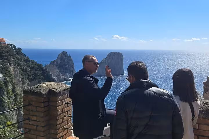 Tourists enjoy a panoramic view of the Faraglioni rock formations on a sunny day during a Capri shore excursion.