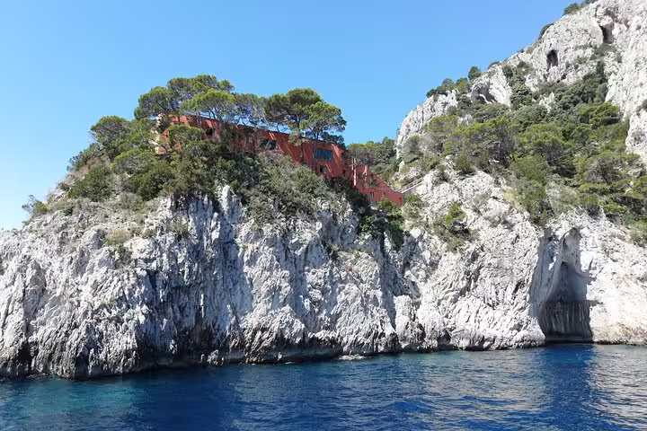 View of the picturesque rocky coastline of Capri with lush greenery and crystal-clear waters beneath a sunny sky.
