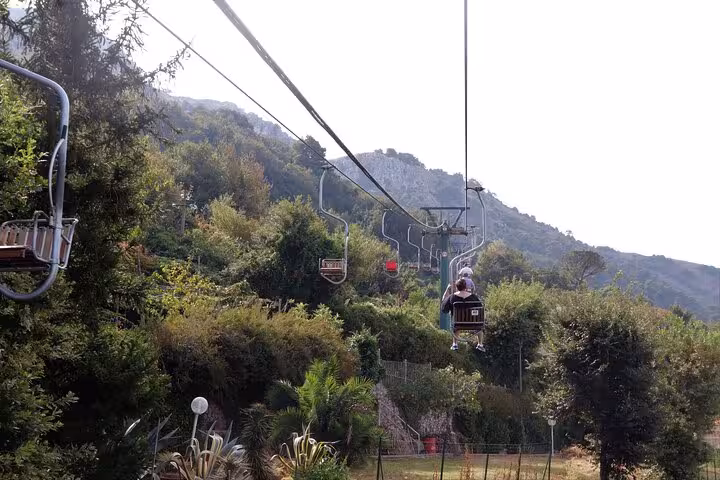 Scenic view of chairlifts ascending through lush greenery and hills, offering stunning vistas on the Capri guided tour.