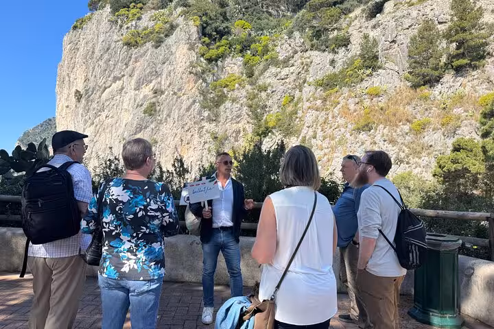 Tour guide leads a group near the rocky cliffs of Capri, sharing insights during the guided tour experience.