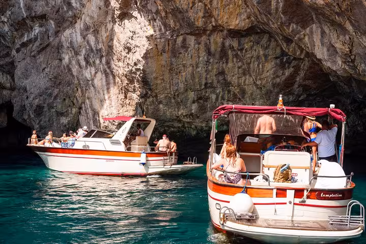 Two boats with tourists exploring a rocky cove on a Capri Island day trip from Sorrento, under sunny skies.