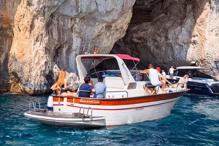 Tourists enjoy a small group boat excursion near the cliffs of Capri Island, departing from Amalfi.
