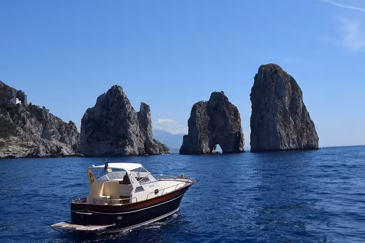 Scenic view of boat cruising near iconic Faraglioni rock formations on Capri Island day excursion from Amalfi.
