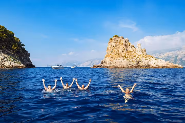 Group swimming joyfully in vibrant blue waters near rocky Capri Island during Amalfi day boat tour.