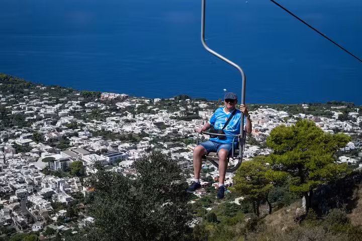 Tourist enjoys panoramic views of Capri from a chairlift ride, part of a guided island exploration.