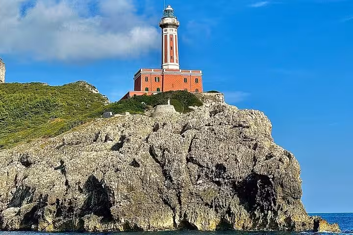 Iconic lighthouse on rocky cliff against blue sky, seen on Capri Island boat tour from Amalfi.