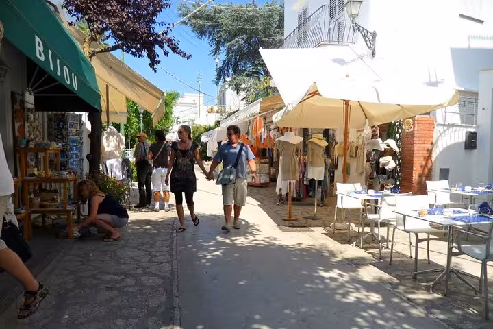 Tourists enjoy shopping in the charming streets of Capri, featuring boutiques and cafes under a sunny sky.