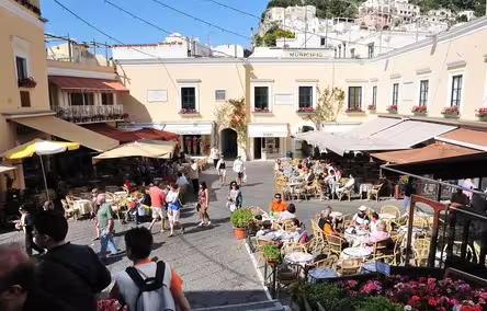 Lively Capri piazza with outdoor cafés, colorful umbrellas and tourists enjoying a sunny Italian island day tour