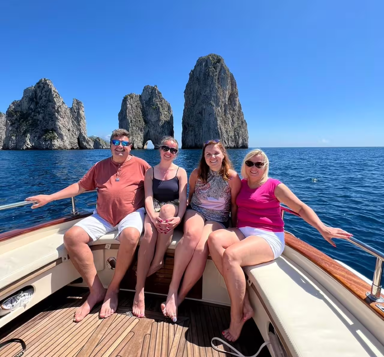 Family relaxing on a private boat tour in Capri with Faraglioni sea stacks behind, ideal for swim stops