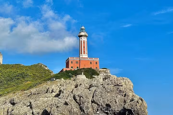 Scenic view of Punta Carena Lighthouse on Capri's rocky coastline under a clear blue sky.