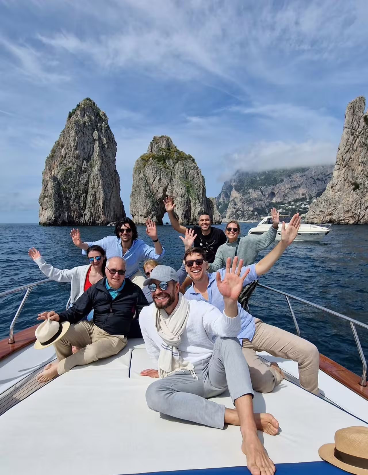 Happy travelers waving on a shared Capri boat excursion near the Faraglioni sea stacks on a sunny day