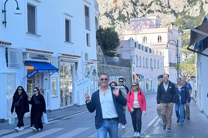 A group of tourists strolls down a charming street in Capri, exploring shops during a guided shore excursion.