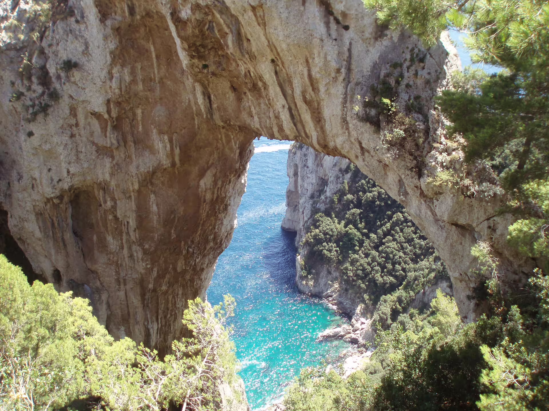 Natural stone arch overlooking turquoise waters and lush cliffs on a hiking stop during a Capri daily tour in Italy