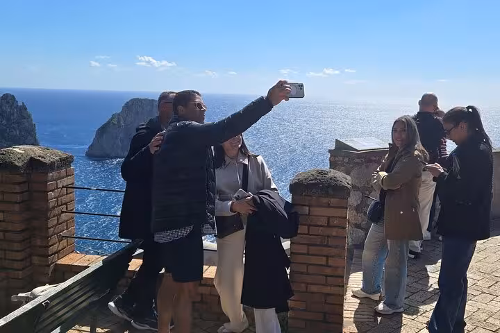 Tourists take a selfie with the stunning Faraglioni rock formations in the background on a sunny Capri tour.