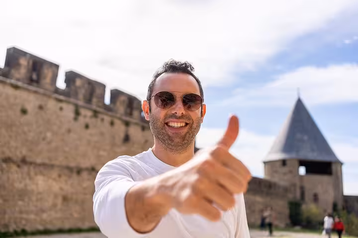 A smiling tourist gives a thumbs-up in front of Carcassonne's ancient fortifications, enjoying a private tour experience.