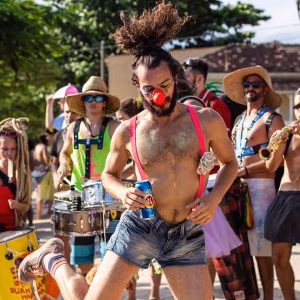 Energetic dancer with red nose and soda can enjoying lively street carnival, surrounded by musicians.