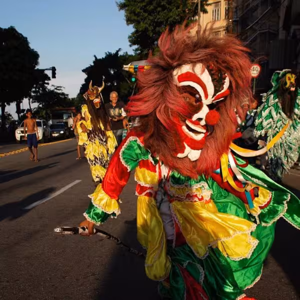 Performer in elaborate costume with a striking mask parading during a vibrant street carnival.