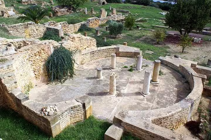 Circular Roman-style ruin with standing columns amidst green landscapes on a Carthage Discovery half-day tour.