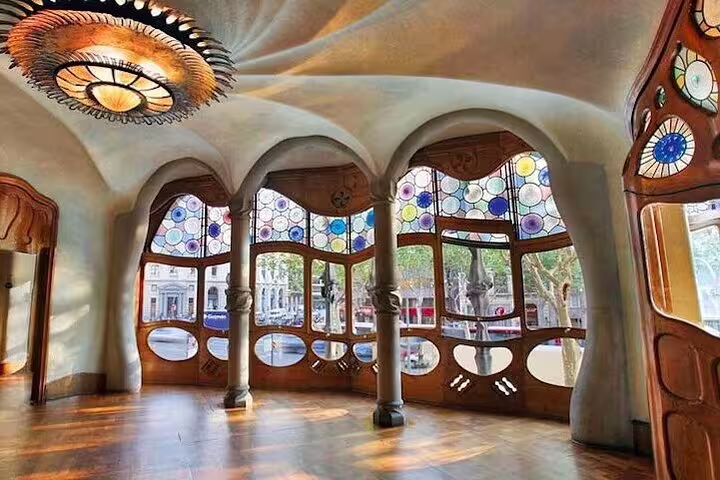 Sunlit interior of Casa Batlló with Gaudí's signature stained glass windows and unique architectural details.