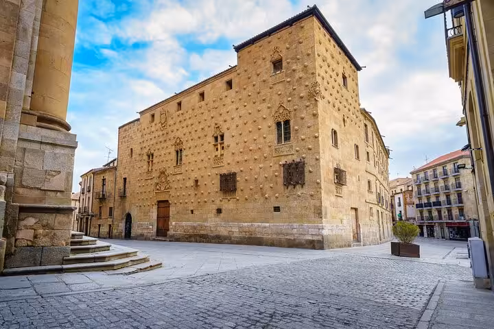 View of the stunning Casa de las Conchas in Salamanca, showcasing its unique shell-adorned facade under a blue sky.