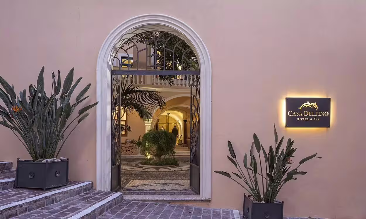 Elegant entrance of Casa Delfino Hotel & Spa in Crete, featuring lush greenery and inviting architectural design.