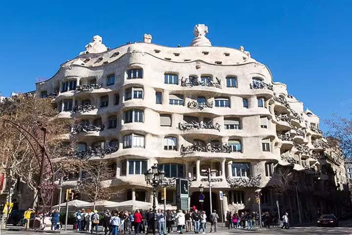 Tourists gather outside Casa Milà, an iconic Gaudí building with a wavy stone facade in Barcelona's Paseo de Gracia.