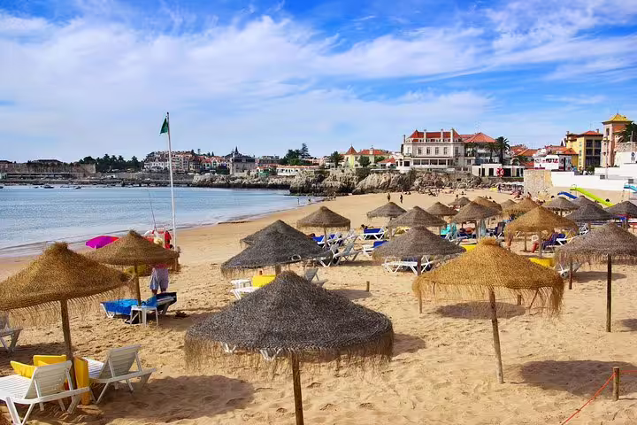 Sunny beach in Cascais with straw umbrellas and scenic coastal view, perfect for a Sintra and Lisbon private day tour.