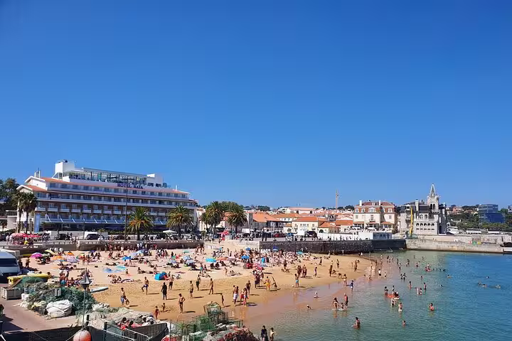 Sunny day at Cascais beach with vibrant crowds, clear blue skies, and picturesque seaside views on a Sintra-Cascais tour.