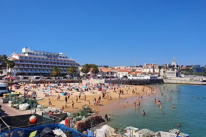 Sunny Cascais beach bustling with tourists enjoying the sandy shores and clear waters on a vibrant summer day.