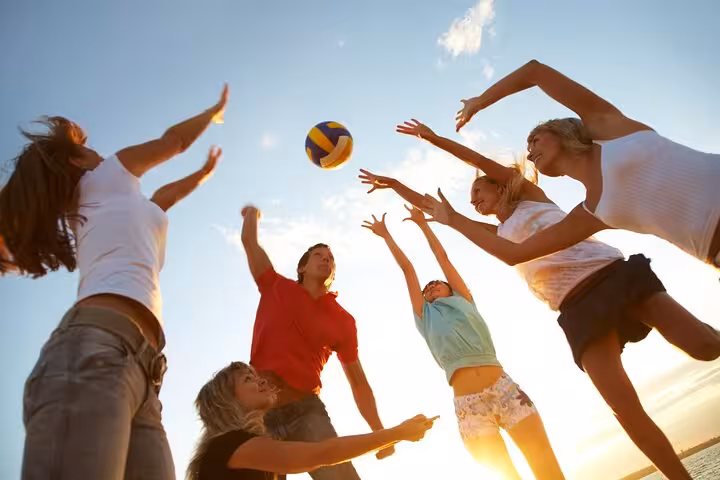 Group of friends play beach volleyball under a clear blue sky in Cascais, Portugal.