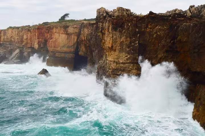 Dramatic ocean waves crash against the rugged cliffs of Cascais, a highlight of the Sintra and Cascais full-day tour experience.