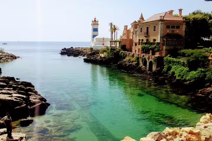 Scenic view of Cascais coast with a historic lighthouse and charming villas, featured in Sintra World Heritage and Cascais Village Tour.