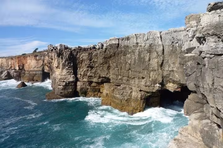 Majestic coastal cliffs with turquoise waves crashing below, showcasing the natural beauty of Cascais on a private tour.