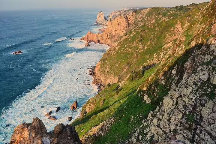 Stunning coastal cliffs of Cascais bathed in sunlight, featured in the Sintra & Cascais full-day tour with Pena Palace visit.