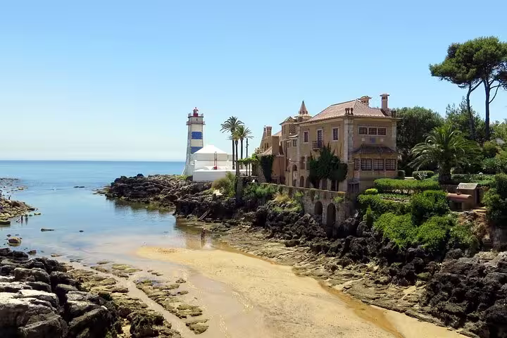 Scenic view of Cascais coastline featuring a historic villa and lighthouse, part of the Sintra and Cabo da Roca full-day tour.